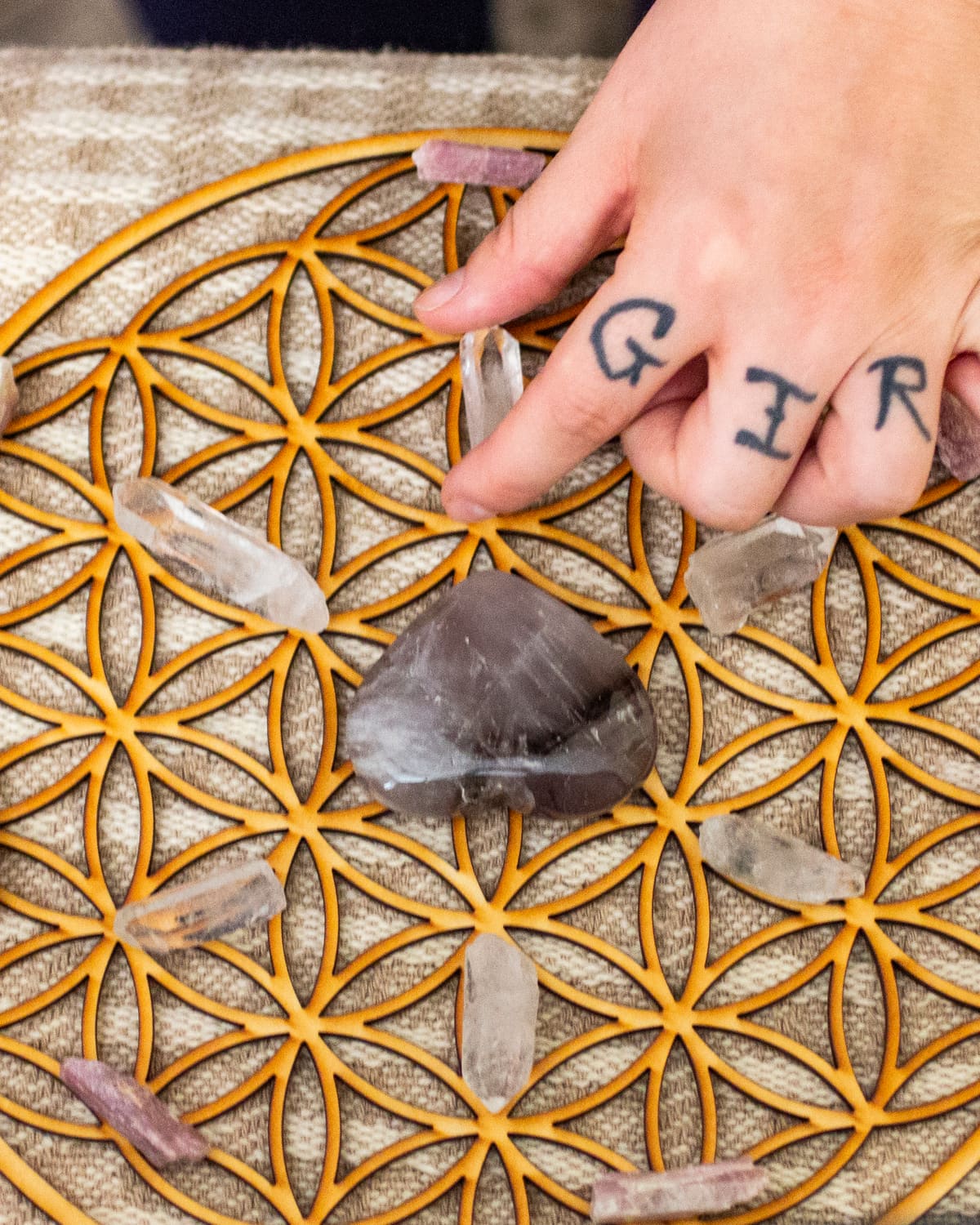 Hands placing crystals on a wooden flower-of-life grid